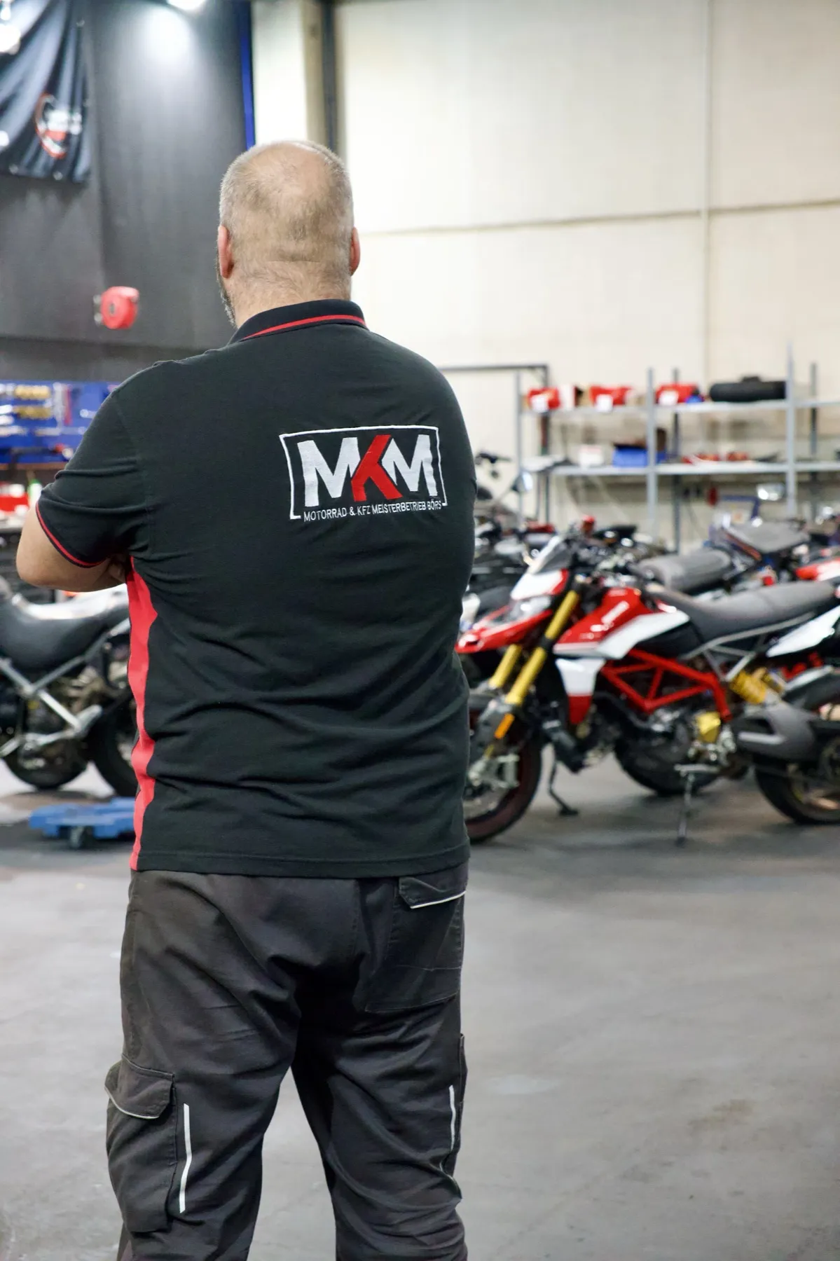 Mitarbeiter von MKM Börs im Shirt mit gesticktem Logo vor Motorrädern in der Werkstatt